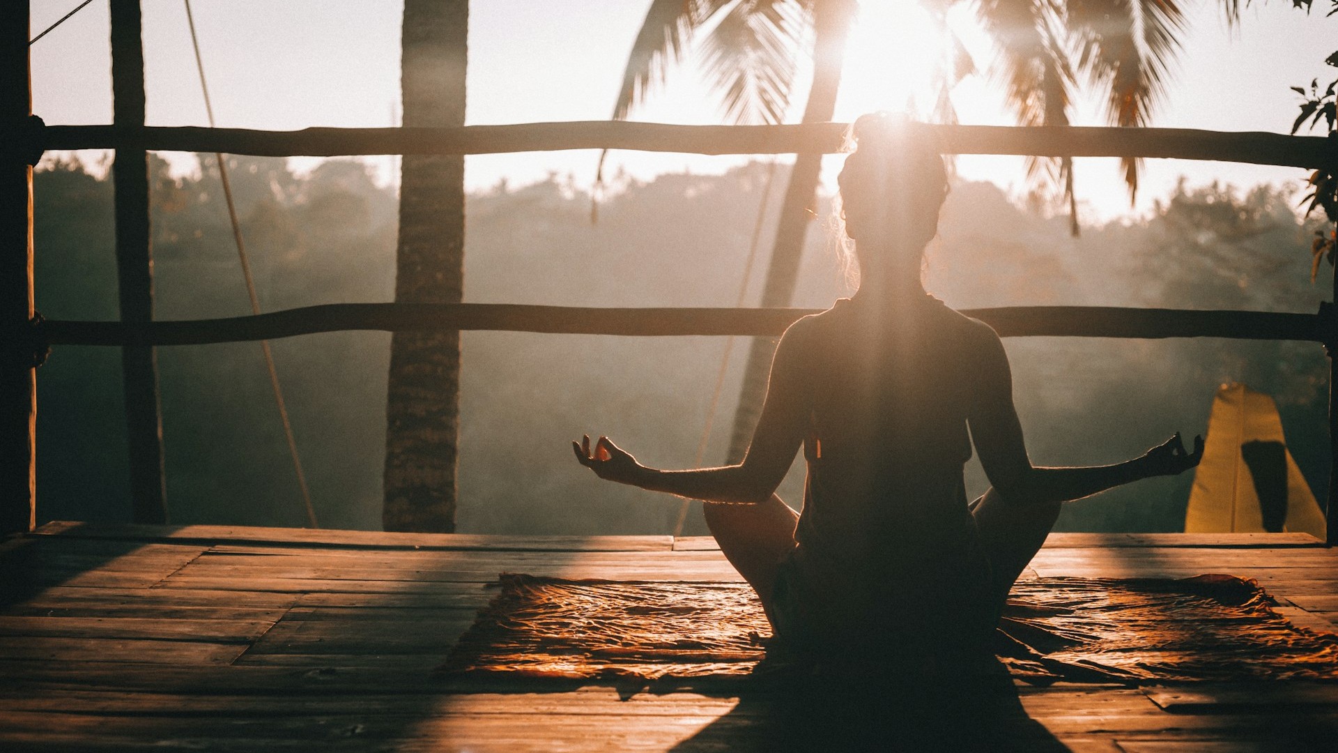 Vrouw in lotushouding tijdens zonsopgang op een houten terras &ndash; rust en focus in lifestyle.