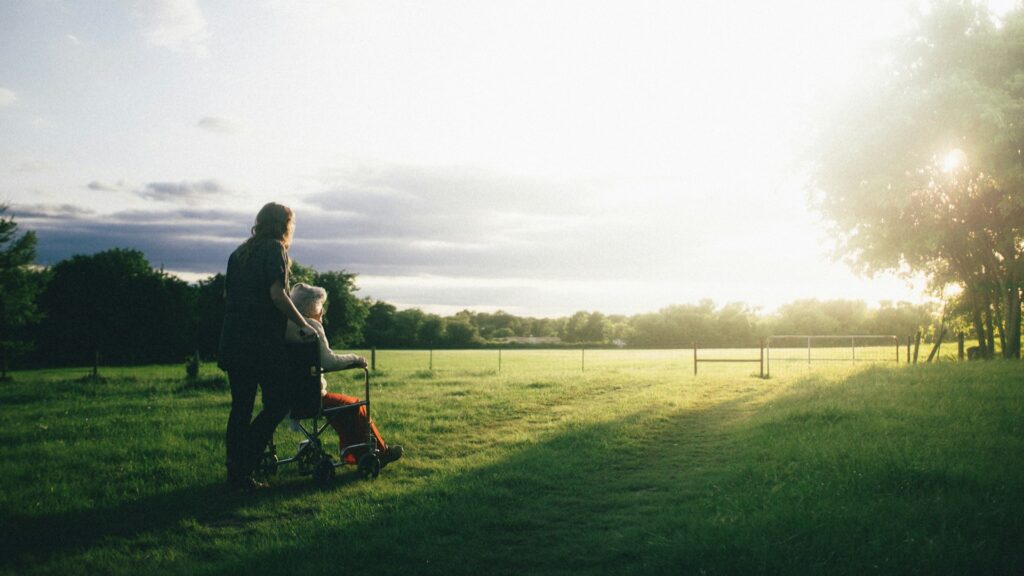 Persoon die een oudere vrouw in rolstoel helpt tijdens wandeling als ondersteuning bij zelfstandig wonen