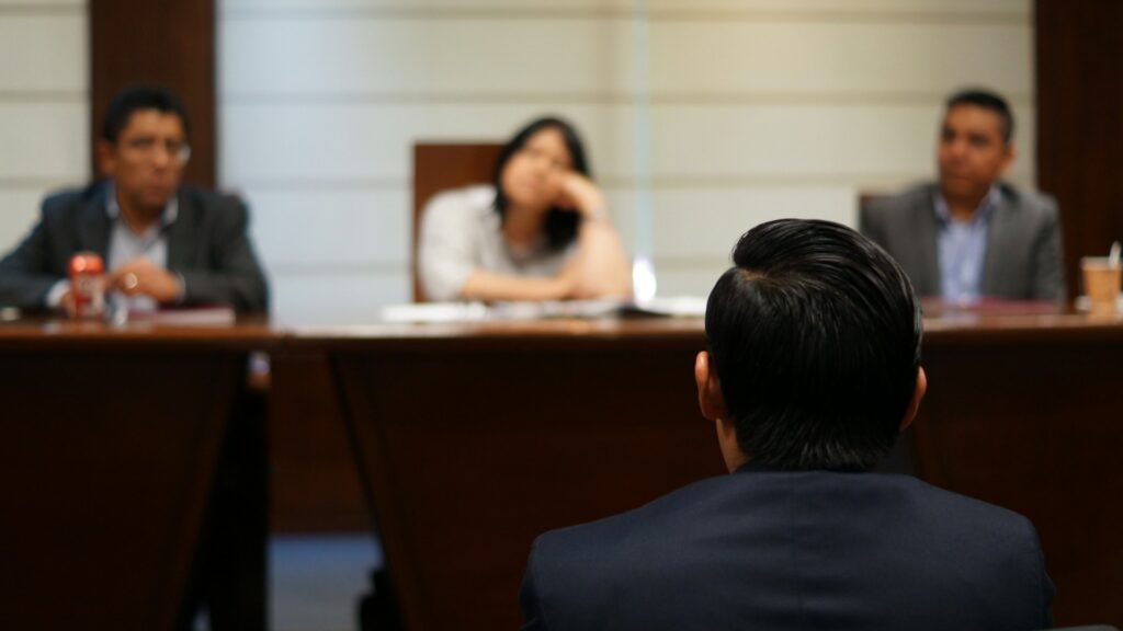 Persoon tegenover rechters in rechtszaal tijdens procedure met zichtbare rechtszaak mentale impact