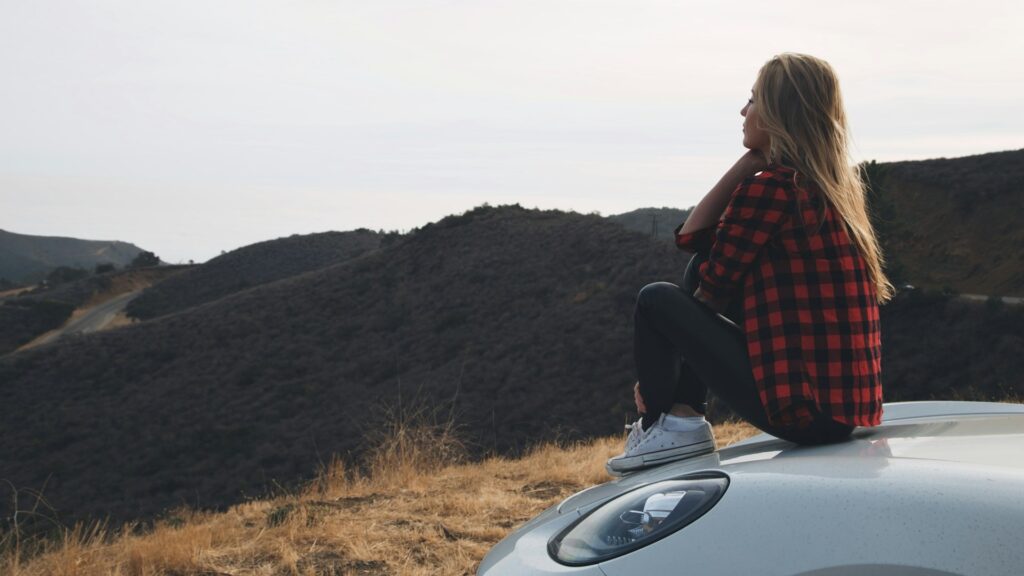 Vrouw zit op auto en kijkt uit over landschap, passend bij vrijheid en flexibiliteit in flexibele werkagenda